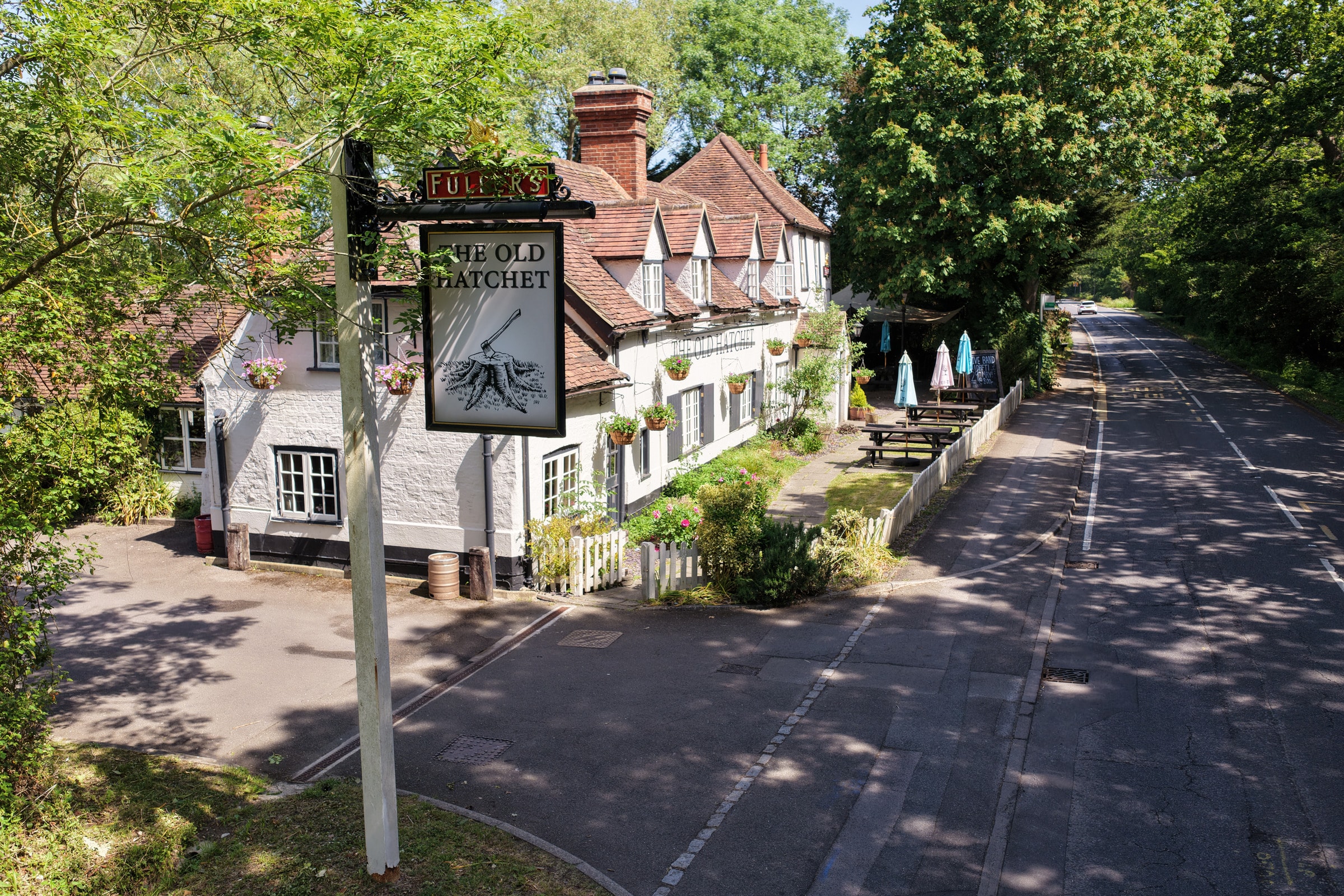 The Old Hatchet pub beside a tree-lined road, with outdoor seating and hanging baskets